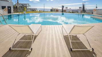 A swimming pool with two lounge chairs and a tiled deck.