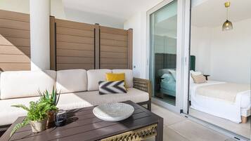 A modern living area with a sofa, a coffee table, and a sliding glass door leading to a bedroom.