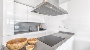 A modern kitchen with white cabinets, a black induction cooktop, and wooden bowls on the counter. - iloftmalaga Panoramica II - El Higueron (Fuengirola)