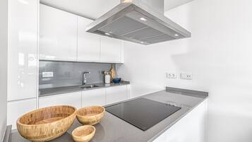A modern kitchen with white cabinets, a black induction cooktop, and wooden bowls on the counter.