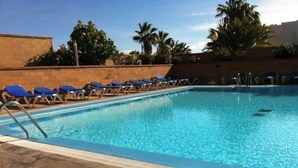 Une piscine à l’eau bleue, entourée de chaises longues et de palmiers.