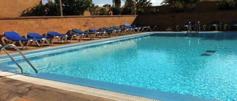 Una piscina con acqua azzurra, circondata da lettini e palme.