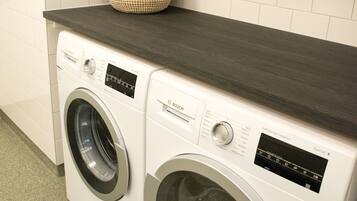 A laundry area with two front-loading washing machines, a dark countertop, and a white tiled wall.