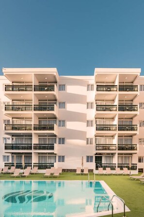 A modern hotel with multiple balconies, a swimming pool, and lounge chairs.