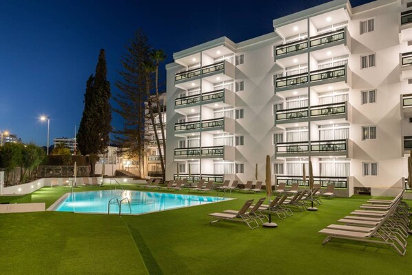 A modern hotel with a swimming pool and sun loungers.