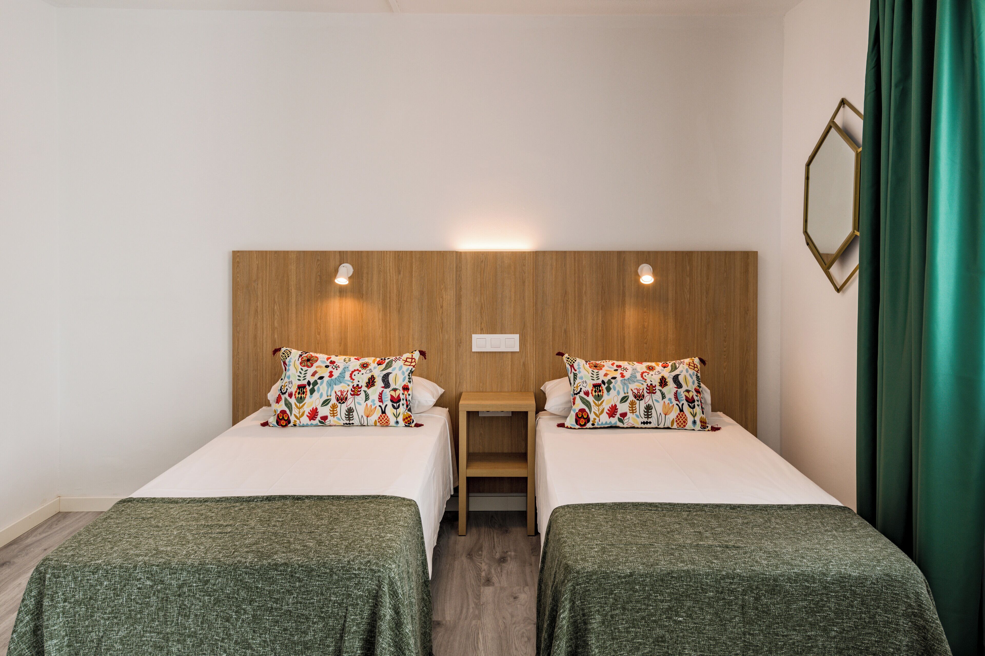 A hotel room with two single beds, a wooden headboard, a small table, and a mirror on the wall.