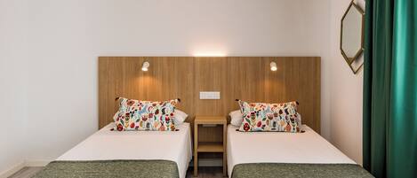 A hotel room with two single beds, a wooden headboard, a small table, and a mirror on the wall.