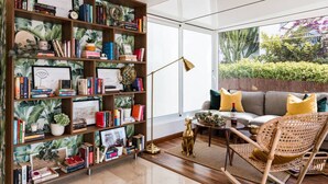 Una sala de estar moderna con una amplia estantería, un sofá con cojines amarillos y una silla de mimbre.