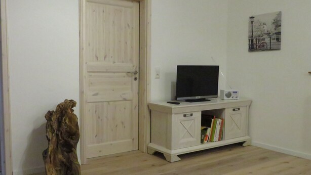 A room with a wooden door, a TV on a cabinet, and a bookshelf.