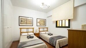 A hotel room with two single beds, a wooden desk, a nightstand, and two framed maps on the wall. - Alcaudon - Isla Canela Beach IAHL59P273 (Isla Canela)