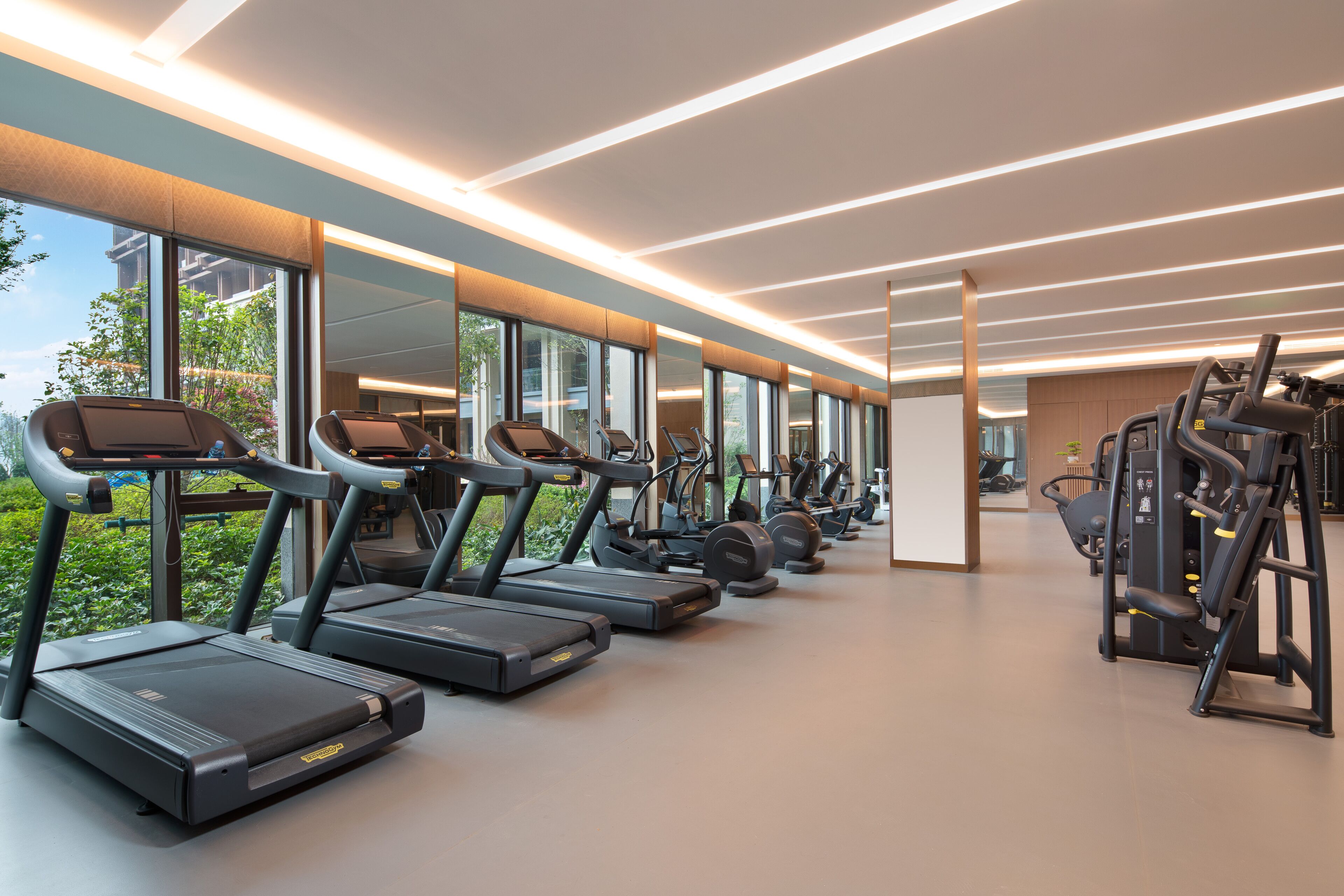 Een moderne sportschool met loopbanden en krachtapparaten, grote ramen en een schoon, goed verlicht interieur.