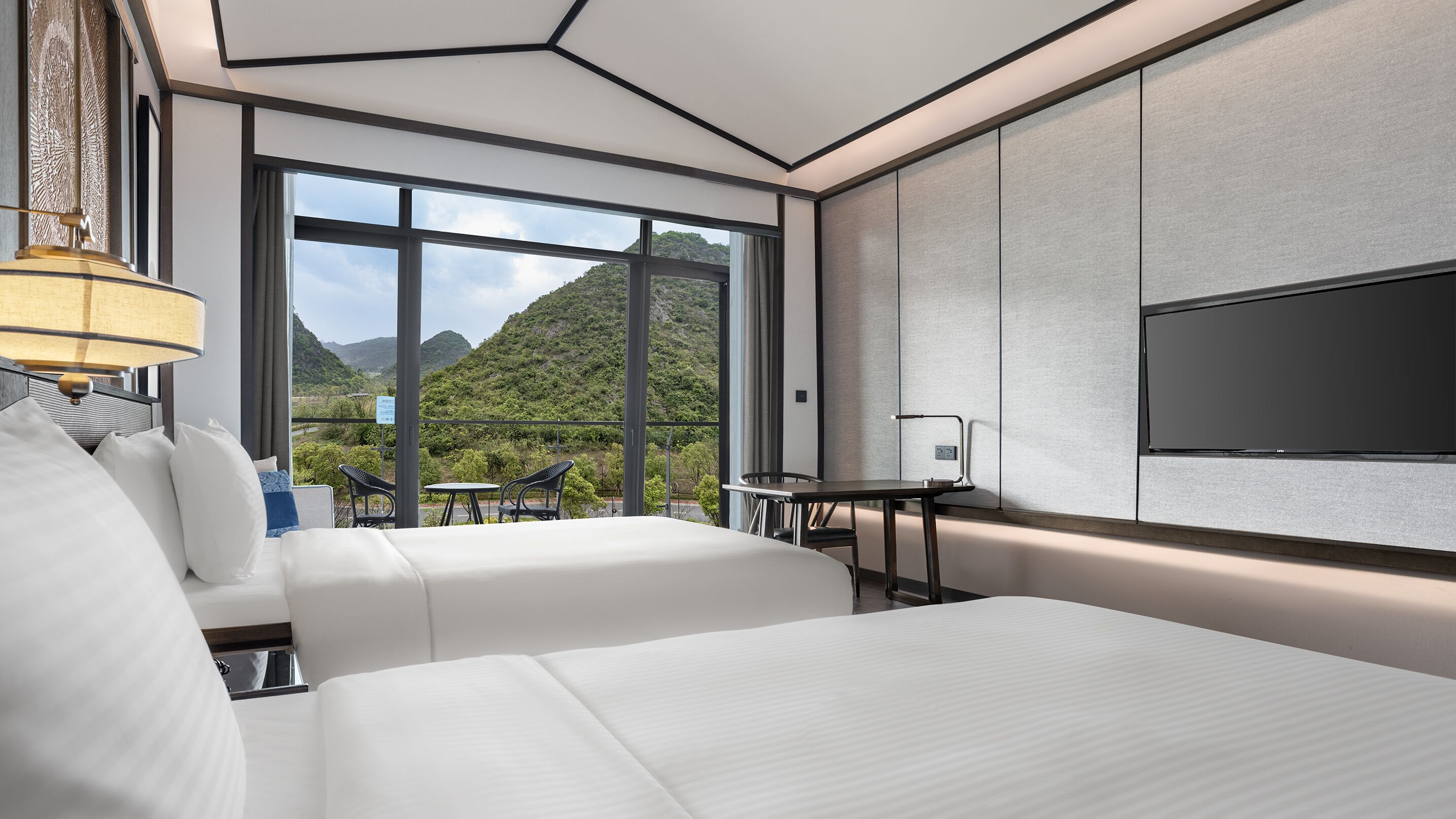 Una habitación de hotel moderna con dos camas, televisión, escritorio y balcón con vistas a la montaña.