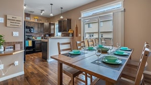 A modern kitchen with dark wooden cabinets, a dining area with a wooden table set for six, and a large window providing natural light.