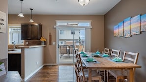 A dining area with a wooden table set for six, a kitchen with dark cabinets, and a view through a glass door to the outside.