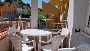 Een terras met een ronde tafel en witte plastic stoelen, omringd door een betegelde vloer en een metalen hekwerk.