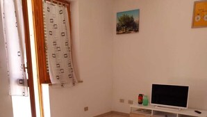 Een woonkamer met een bank, een houten tafel, een televisie op een witte dressoir en een raam met gordijnen.
