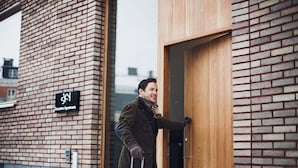 A person entering a building with a brick facade and a wooden door. - Sky Hotel Apartments Hospitalstorget (Linkoping)