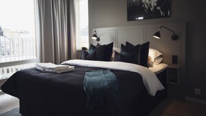 A modern hotel room with a large bed, a view of the city, and a painting on the wall. - Sky Hotel Apartments Hospitalstorget (Linkoping)