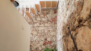 A narrow hallway with a stone wall, a tiled floor, and a staircase with wooden steps. - Suite Bagnara (Syracuse)