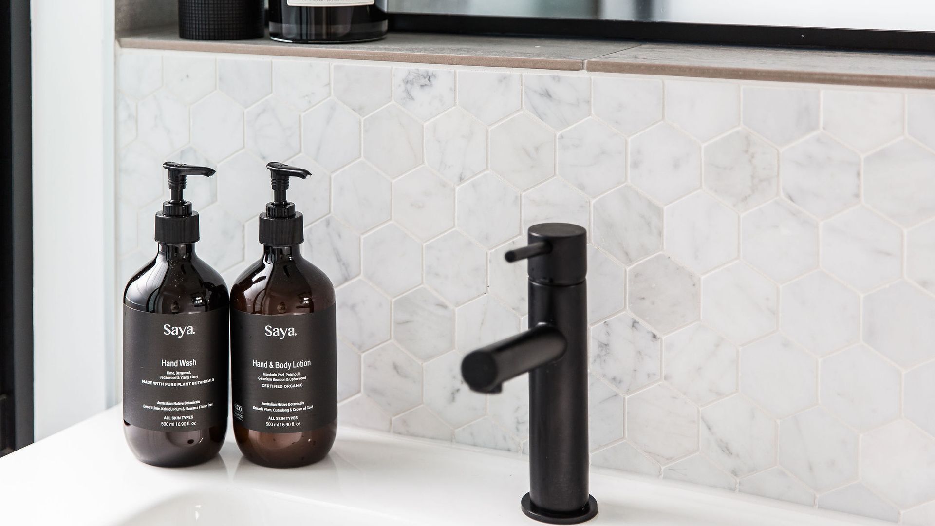 A bathroom sink with two bottles of hand wash and body lotion, and a black faucet.