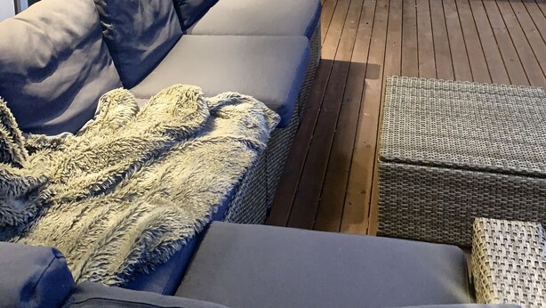 Una terraza techada al aire libre con un sofá, un reposapiés, un banco de madera y una mesita.