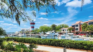 A marina with boats docked, a lighthouse, and buildings with outdoor seating.