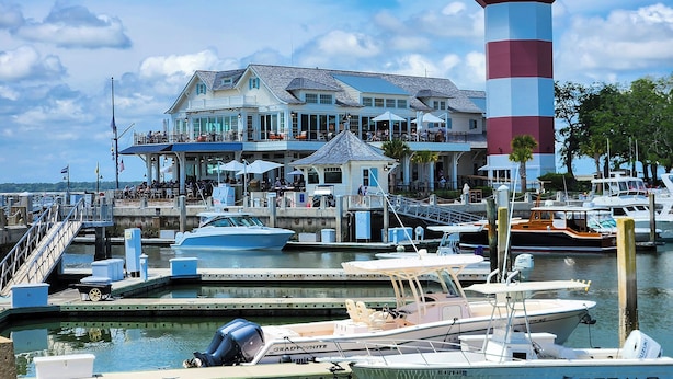 A waterfront building with a lighthouse, docked boats, and a marina.