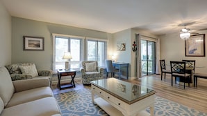 A living room with a sofa, a glass coffee table, a desk, and a dining area with chairs.