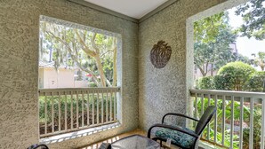 A covered porch with two wicker chairs and a small table, surrounded by white railings and a patterned floor.
