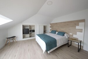 Un dormitorio con techo inclinado, una cama con cabecera de madera, una mesita de noche y estanterías empotradas.