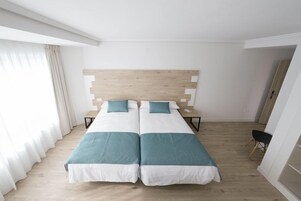 Una cama doble con cabecera de madera, una mesita de noche, una silla y una ventana con cortinas.