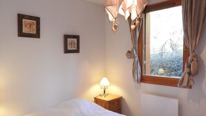 Ein Schlafzimmer mit einem Bett, einem Nachttisch mit Lampe, einem Fenster mit Vorhängen und zwei gerahmten Bildern an der Wand.