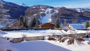 Schneebedeckte Landschaft mit einer Holzhütte und einer Skipiste im Hintergrund.
