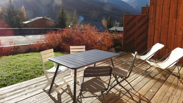 Eine Holzterrasse mit Tisch und Stühlen, mit Blick auf eine gebirgige Landschaft.