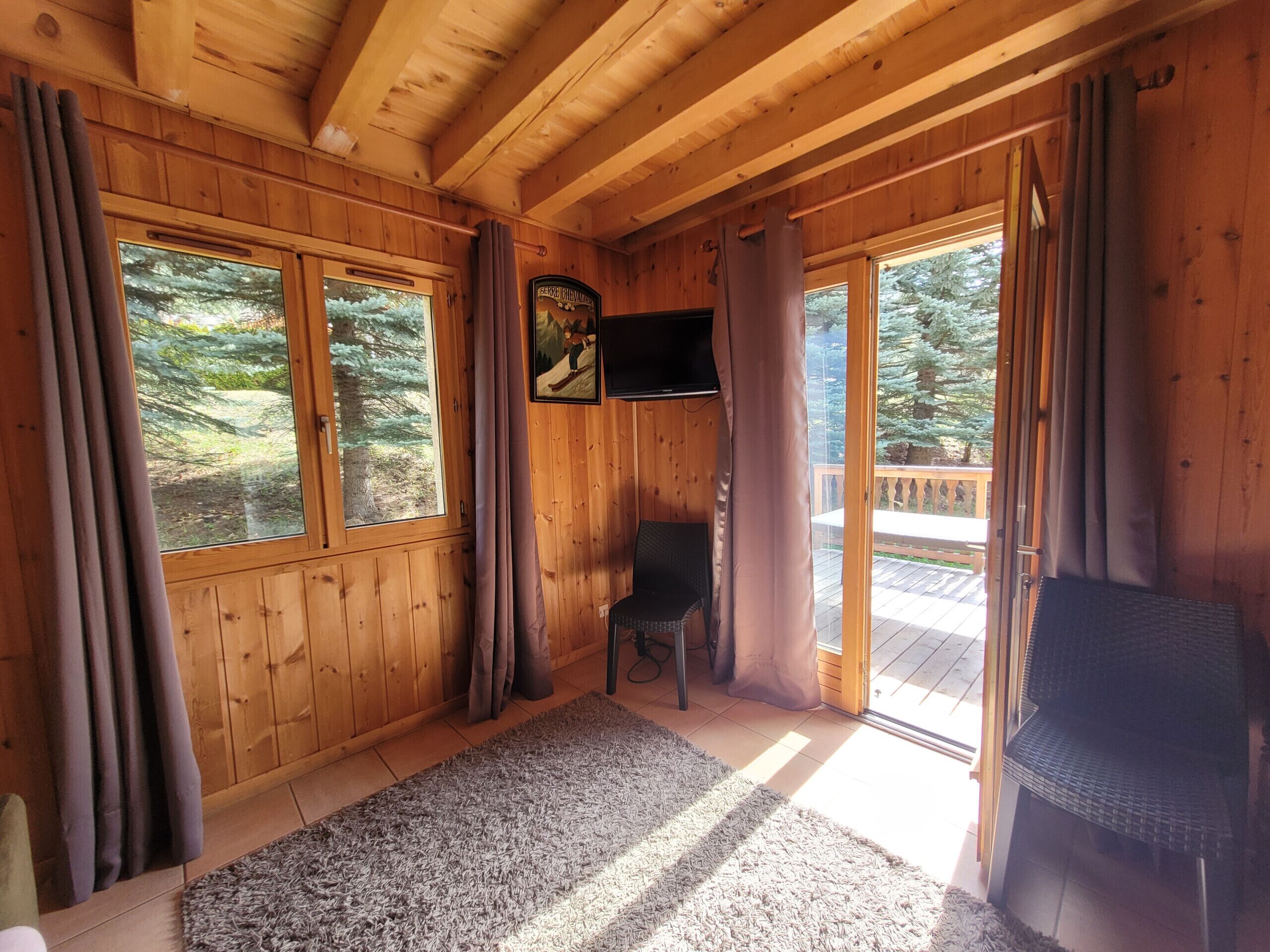A wooden cabin interior with a large window, a television, a chair, and a rug.