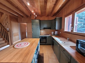A wooden cabin interior with a kitchen, a dining area, and a window with a view of trees.