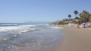 Une plage avec des vagues, un ciel dégagé et quelques personnes.