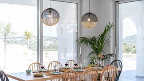 A dining area with a wooden table and chairs, a potted plant, and hanging pendant lights. - Nora Villa in Afandou (Rhodes)