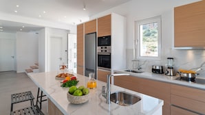 A modern kitchen with a marble countertop, stainless steel appliances, and wooden cabinets. - Nora Villa in Afandou (Rhodes)
