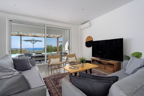 A modern living room with a flat-screen TV, comfortable seating, and a view of the outdoors. - Nora Villa in Afandou (Rhodes)