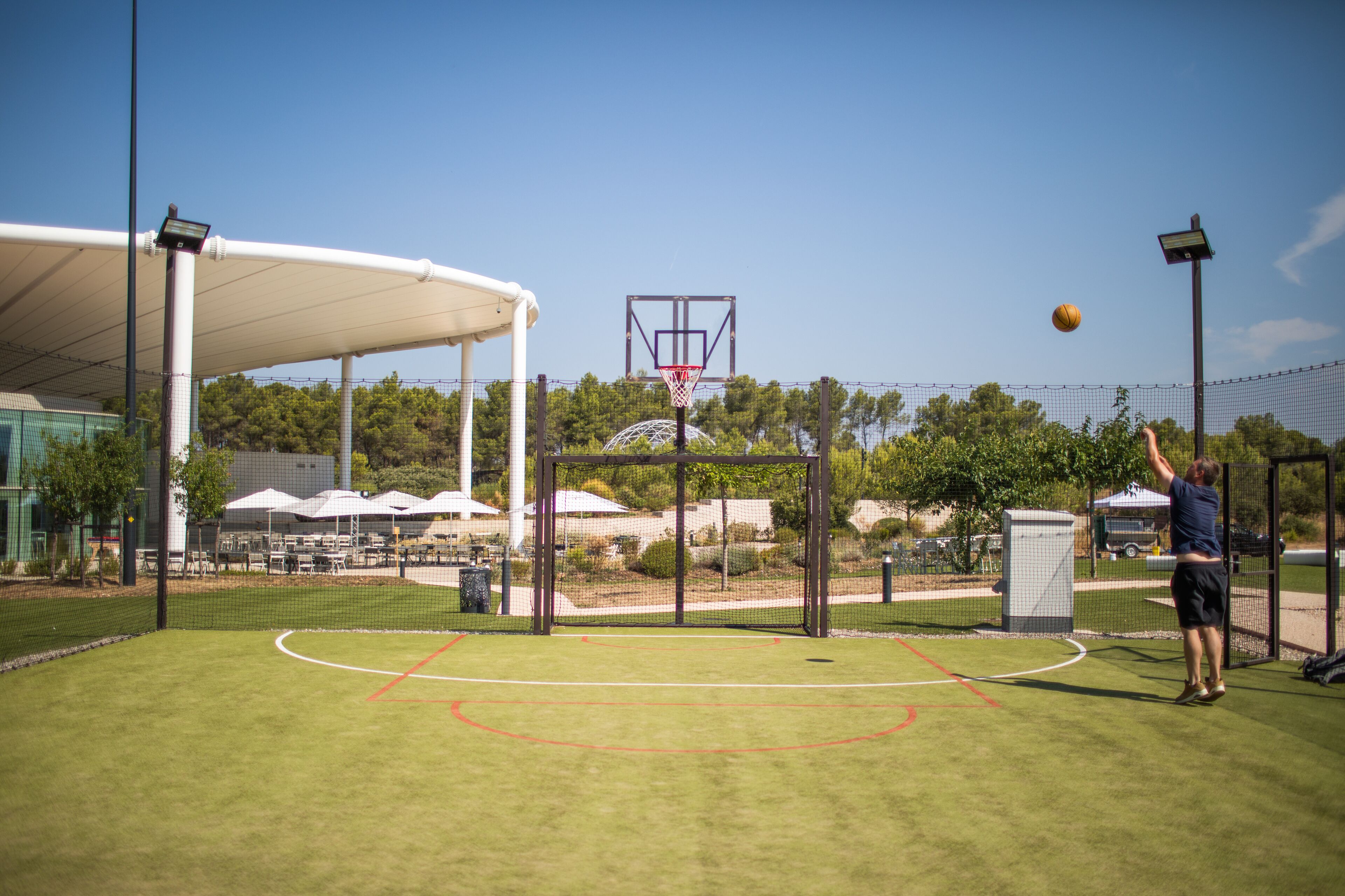 An outdoor basketball court with a hoop, net, and a person playing.