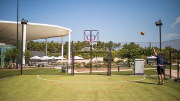 An outdoor basketball court with a hoop, net, and a person playing.
