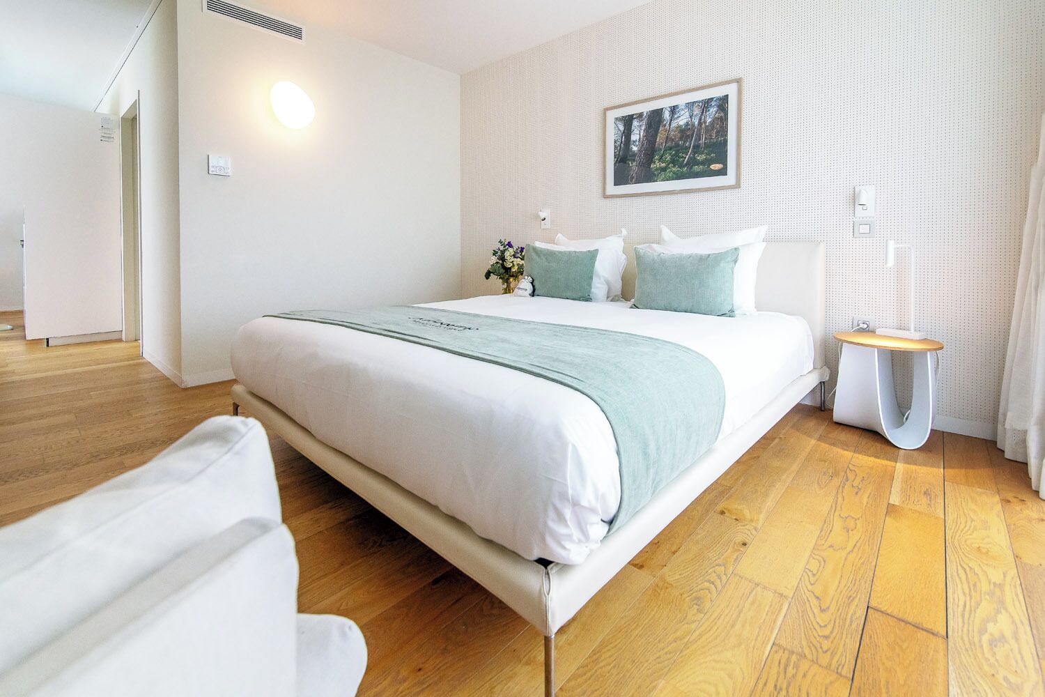 Un dormitorio moderno con una cama grande, una mesita de noche, un cuadro en la pared y suelo de madera.