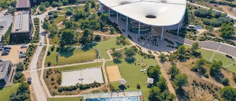 An aerial view of a stadium with a large central field, surrounded by parking areas and greenery.