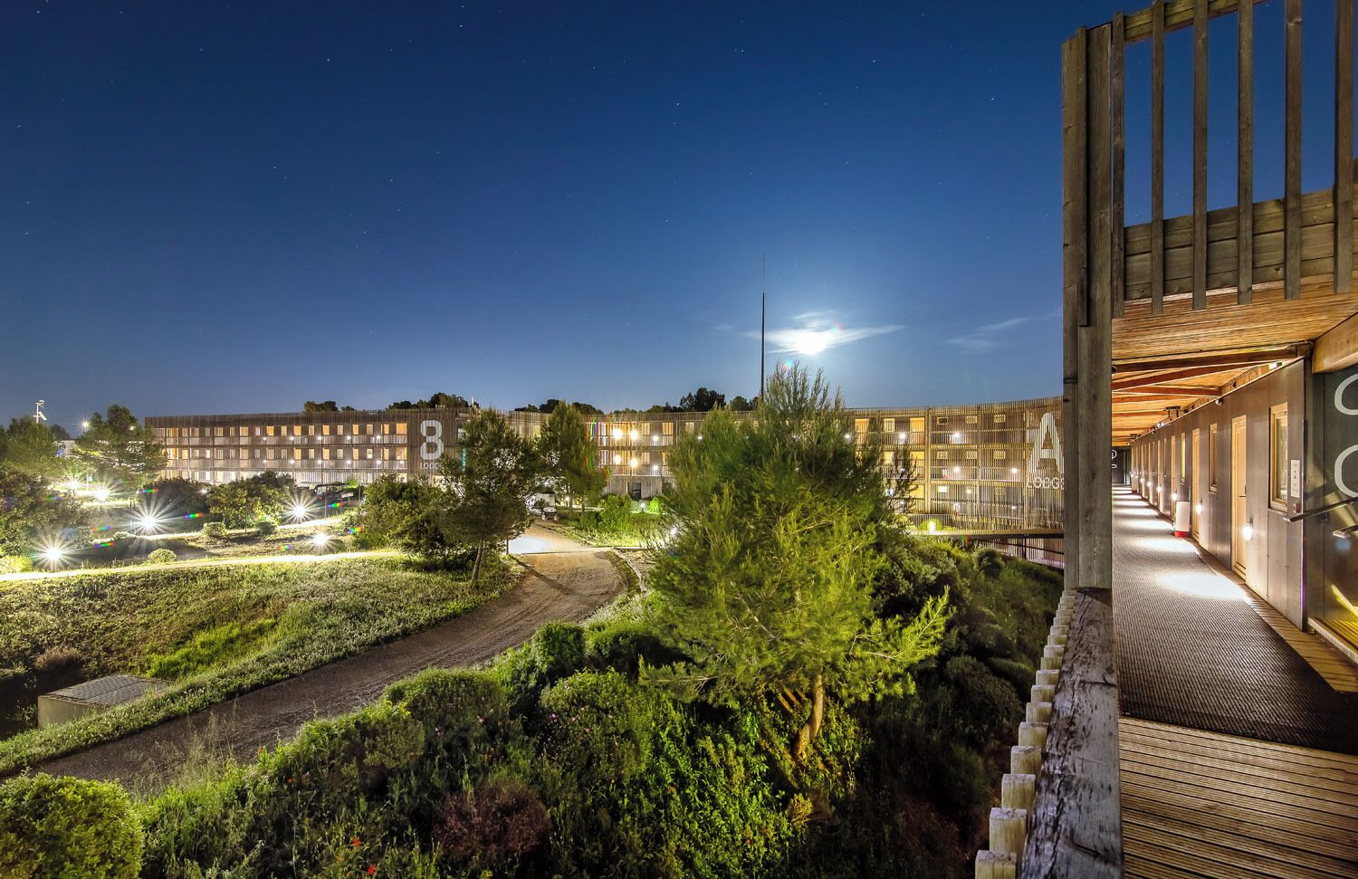 Un hôtel au design moderne, doté d’un chemin bien éclairé, de jardins aménagés et offrant une vue sur la façade de l’immeuble.