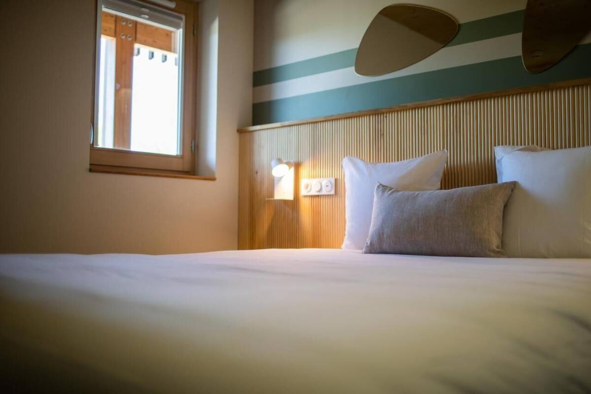 Ein Hotelzimmer mit einem großen Bett, einem Fenster mit Jalousien, einer Wandleuchte und einem gestreiften Wanddesign.