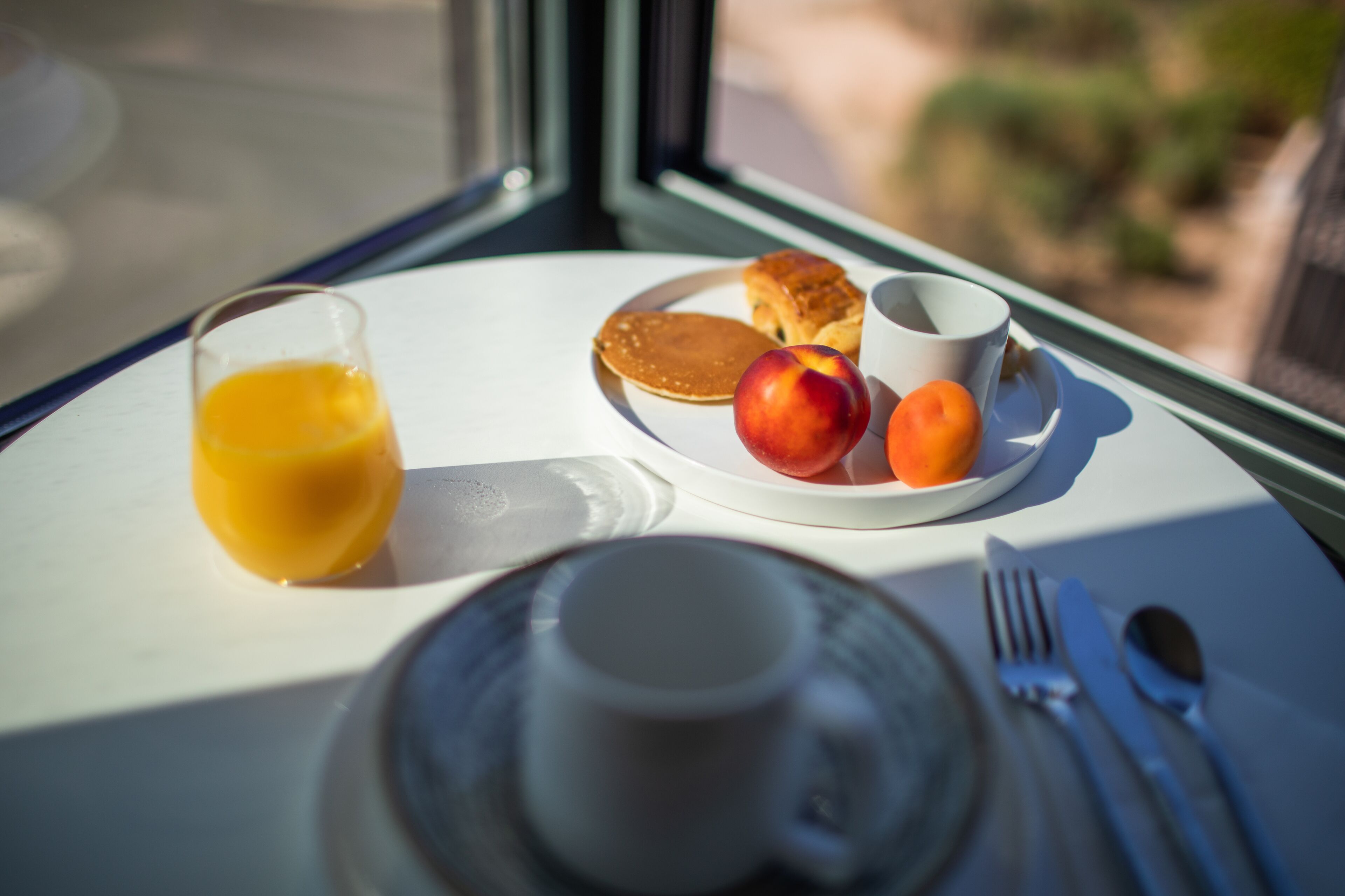 Een ontbijttafel met een glas sinaasappelsap, een bord pannenkoeken, fruit en een kopje.