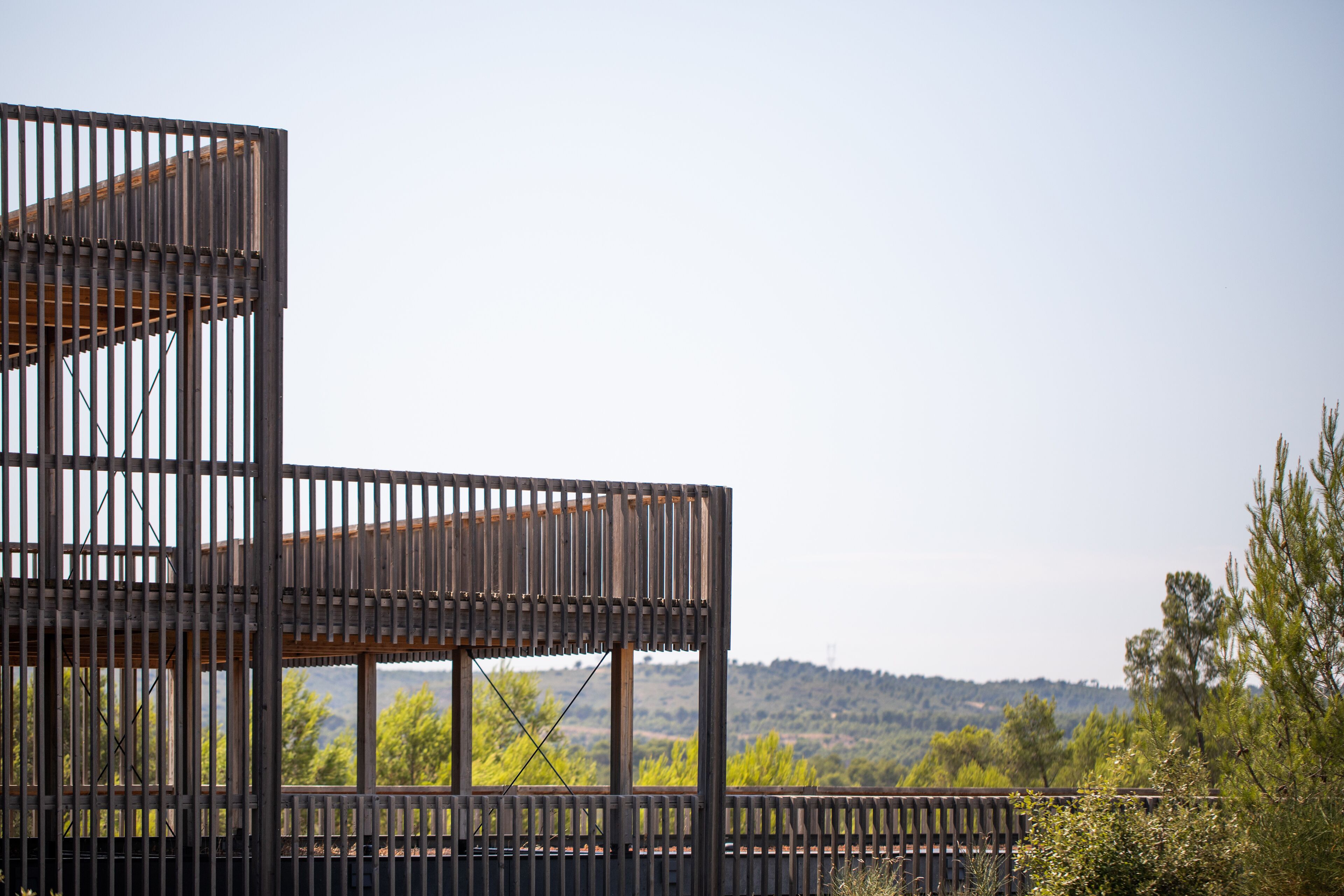 A modern building with a wooden facade and large windows, set against a backdrop of trees and hills.