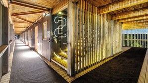 Un pasillo con techo y paredes de madera, una puerta de metal con un logotipo, y vistas al exterior con vegetación.