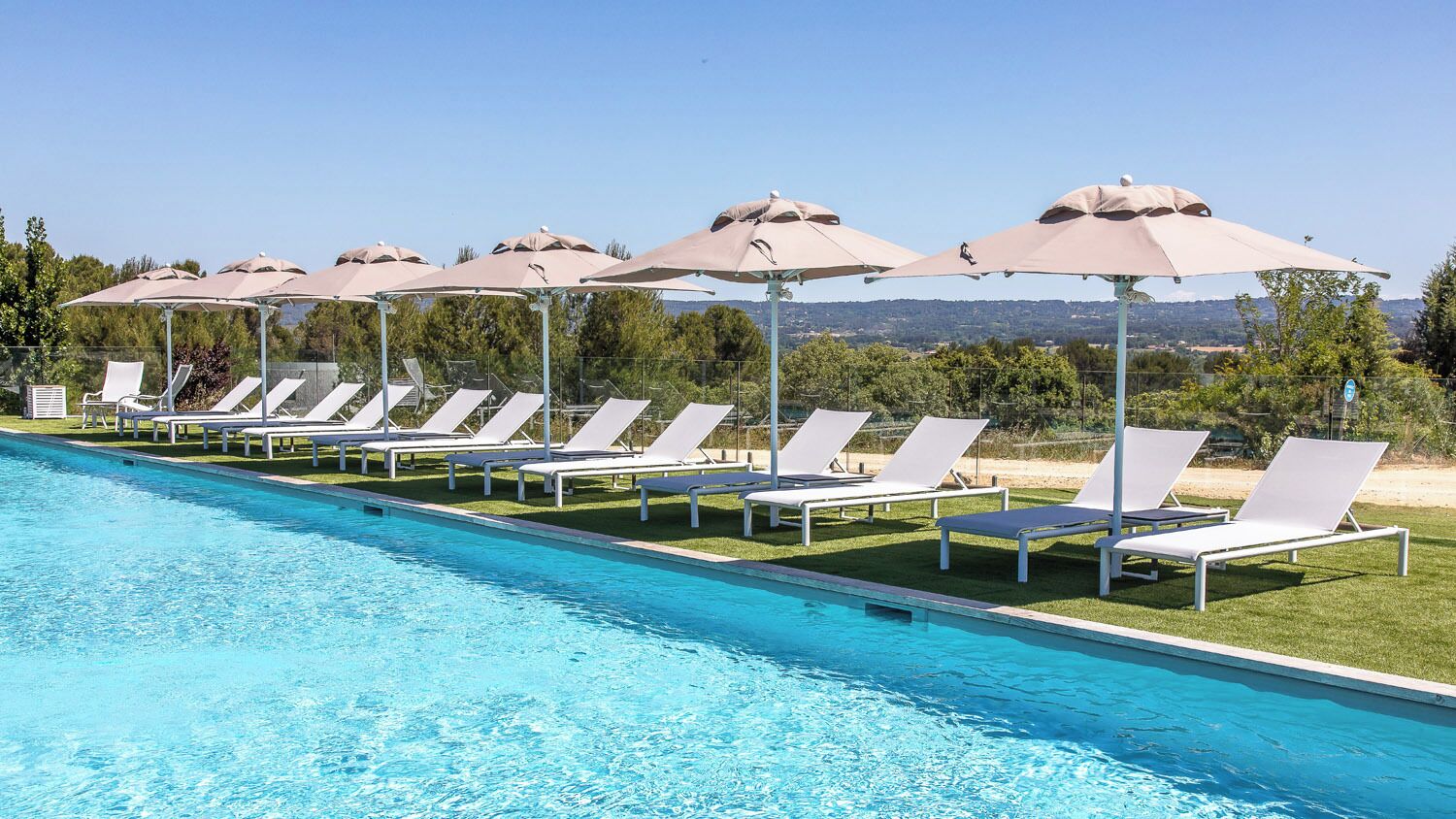 A poolside area with lounge chairs and umbrellas, a clear blue pool, and a view of the landscape.
